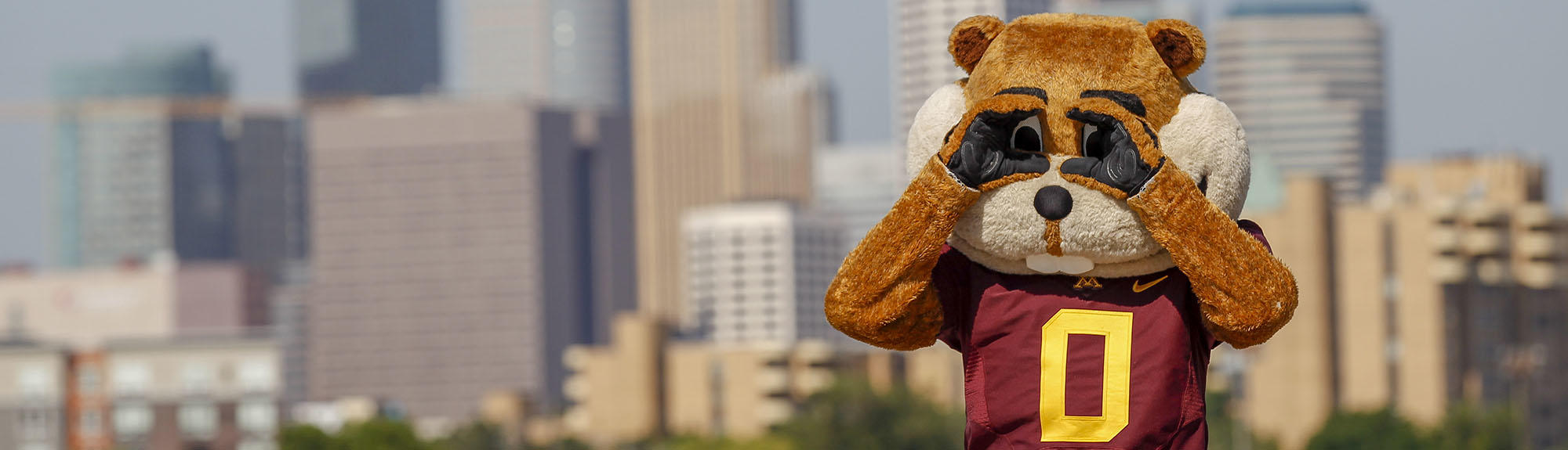 Goldy Gopher uses his hands as binoculars